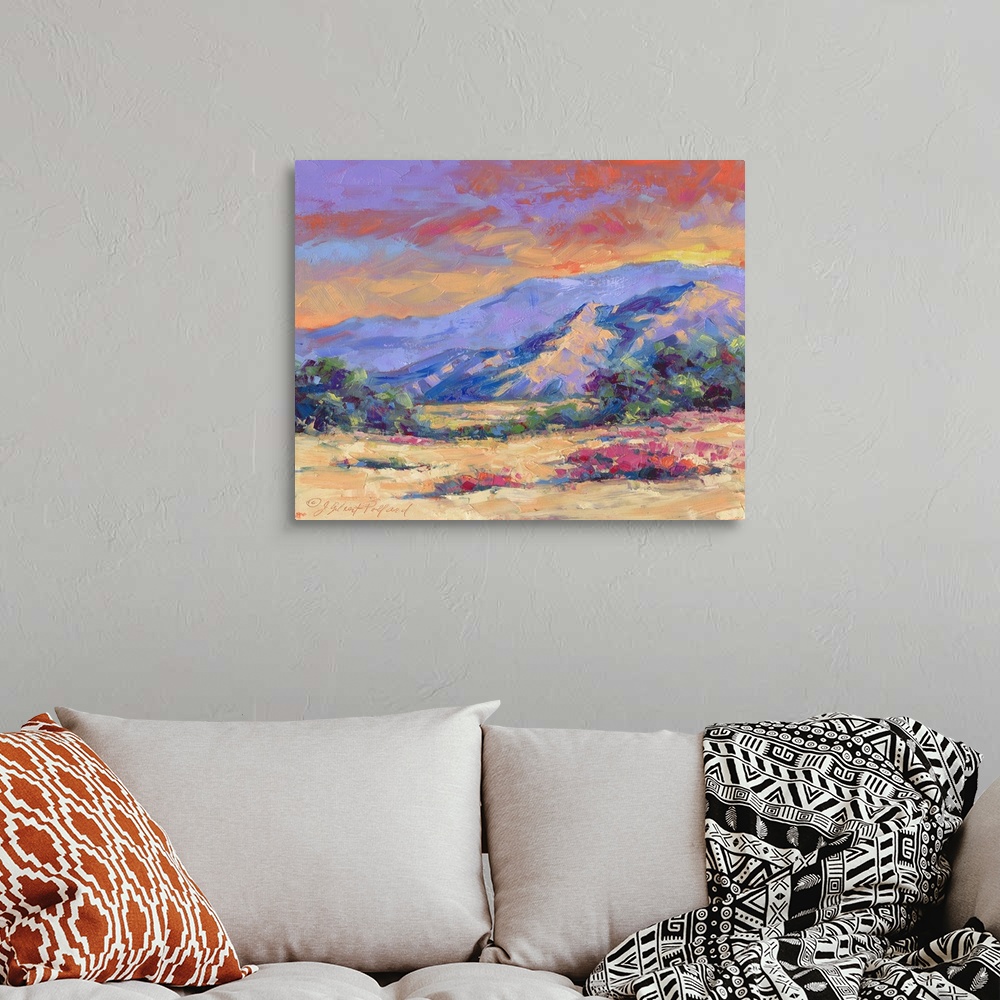 A bohemian room featuring Contemporary vibrant landscape painting of a desert mountain sunset.