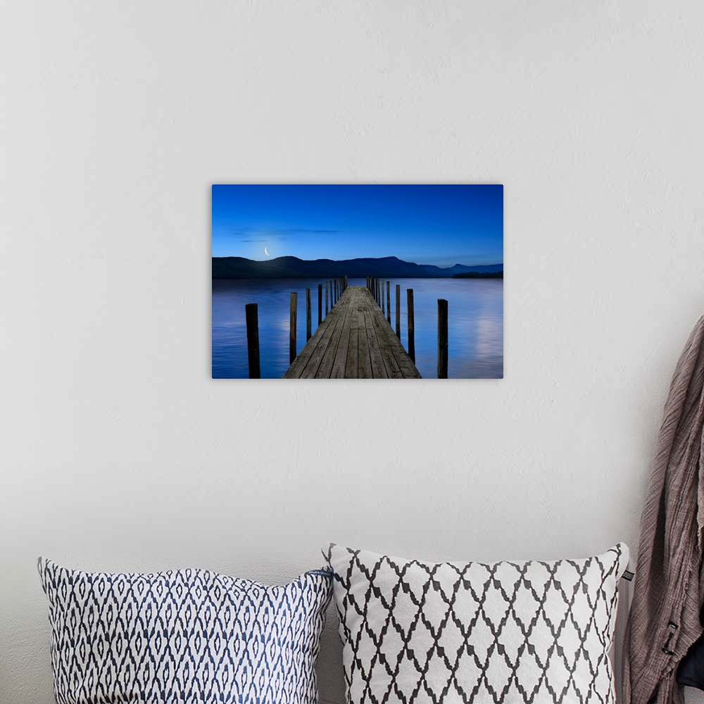 A bohemian room featuring This atmospheric photo features an empty dock reaching out into a serene lake with a crescent moo...