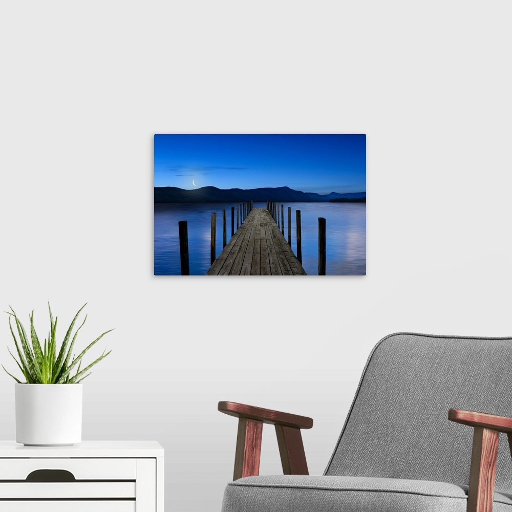 A modern room featuring This atmospheric photo features an empty dock reaching out into a serene lake with a crescent moo...