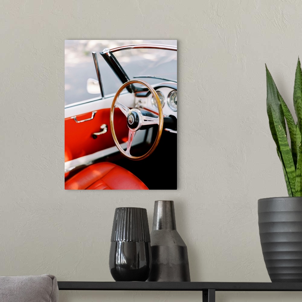A modern room featuring A photograph of the steering wheel and interior of an antique convertible sports car with red lea...