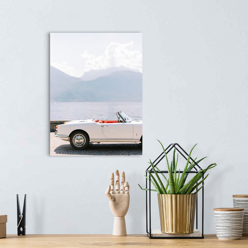 A bohemian room featuring A photograph of the exterior of a white antique convertible sports car with red leather interior,...