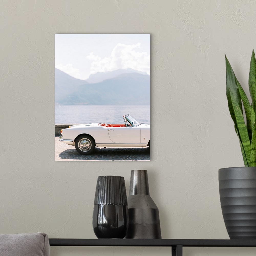 A modern room featuring A photograph of the exterior of a white antique convertible sports car with red leather interior,...