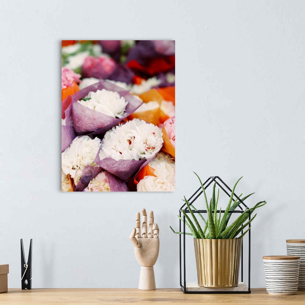 A bohemian room featuring Photograph of bunches of white peony flowers crapped in tissue paper in a market.