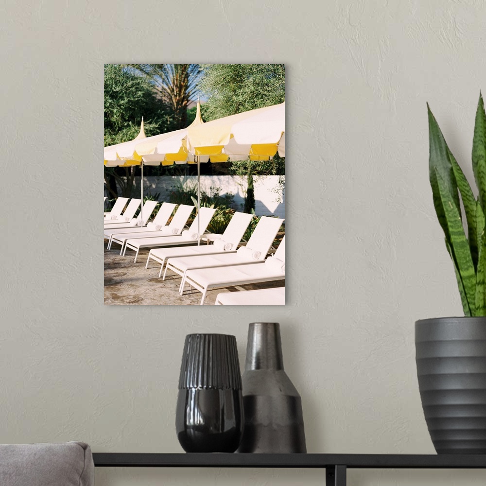 A modern room featuring Photograph of a neat row of pool loungers with rolled towels underneath yellow umbrellas.
