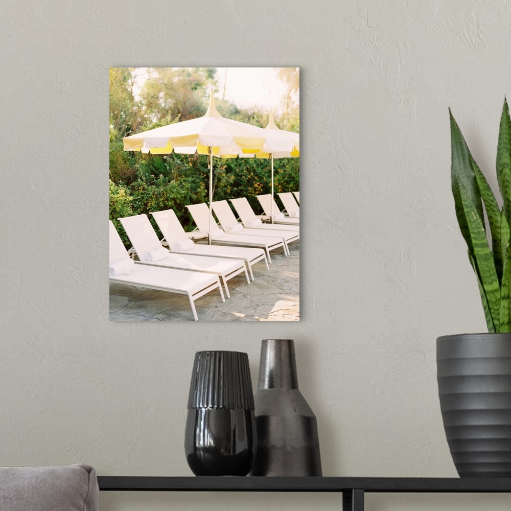 A modern room featuring A photograph of a neat row of pool loungers with rolled towels underneath yellow umbrellas.