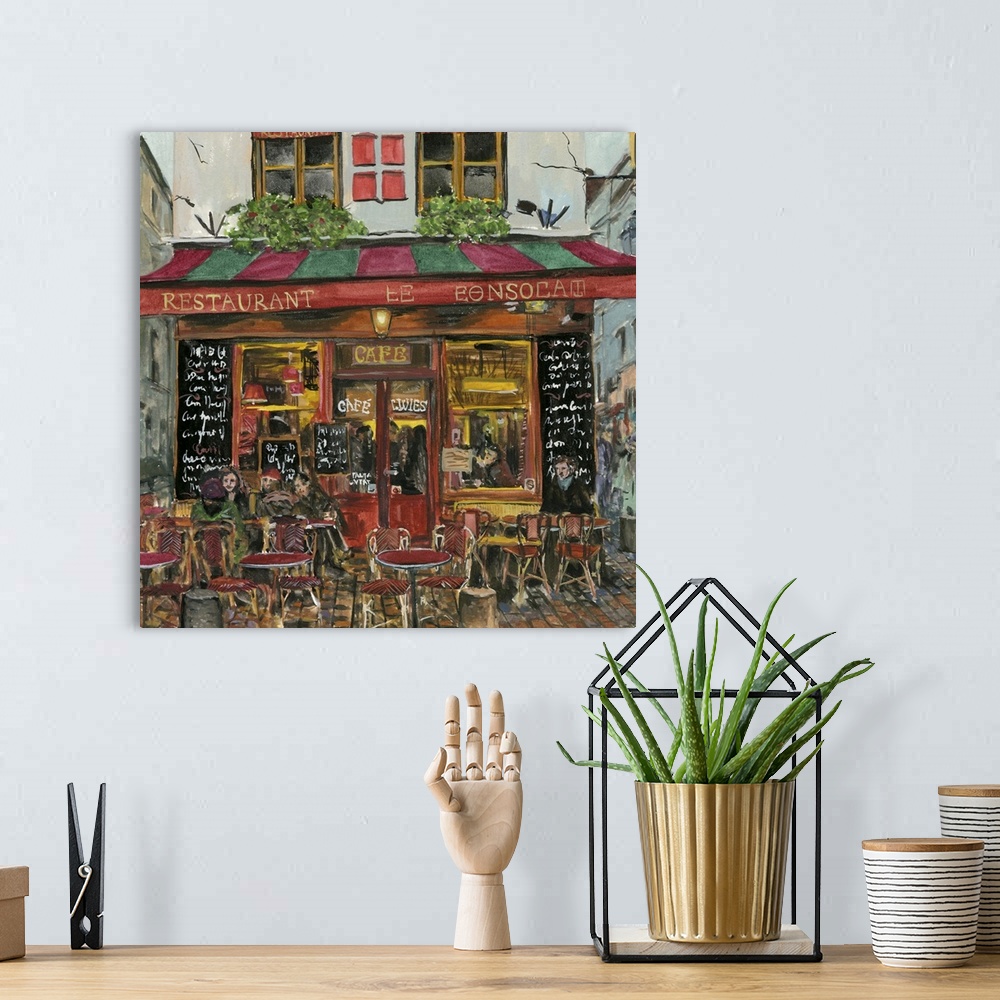 A bohemian room featuring A square decorative image of people sitting outside a red and green cafe in France.