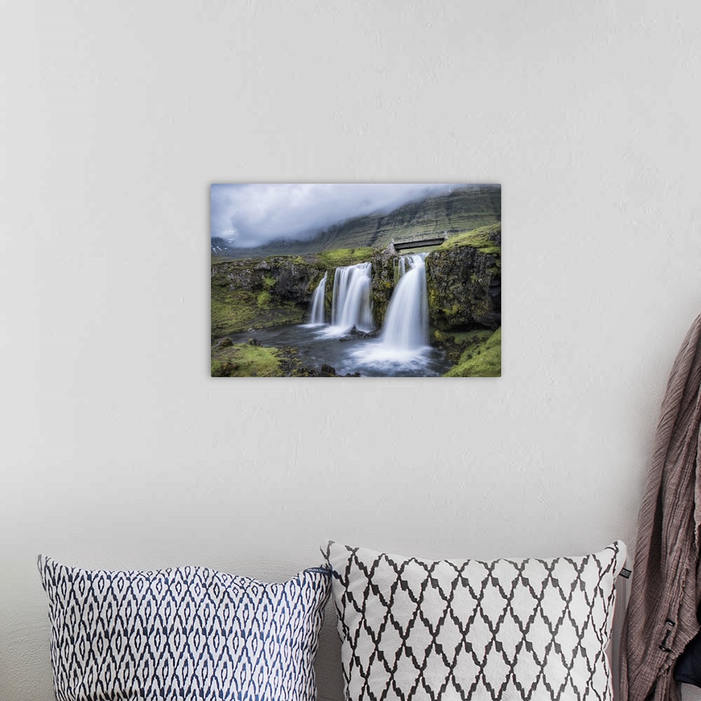A bohemian room featuring Photograph of waterfalls from a river pouring into a small pool with a worn bridge and mountains ...