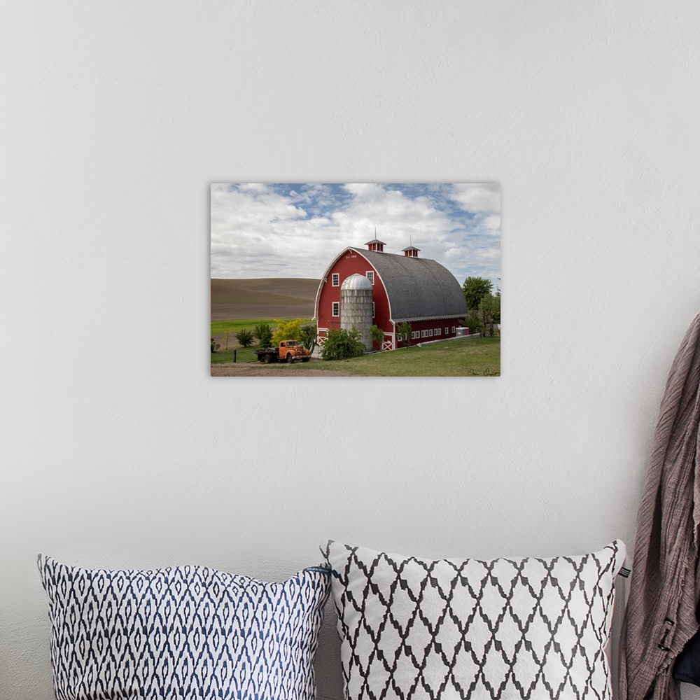 A bohemian room featuring A photograph of a large red barn and grain silo with a vintage orange truck parked out front