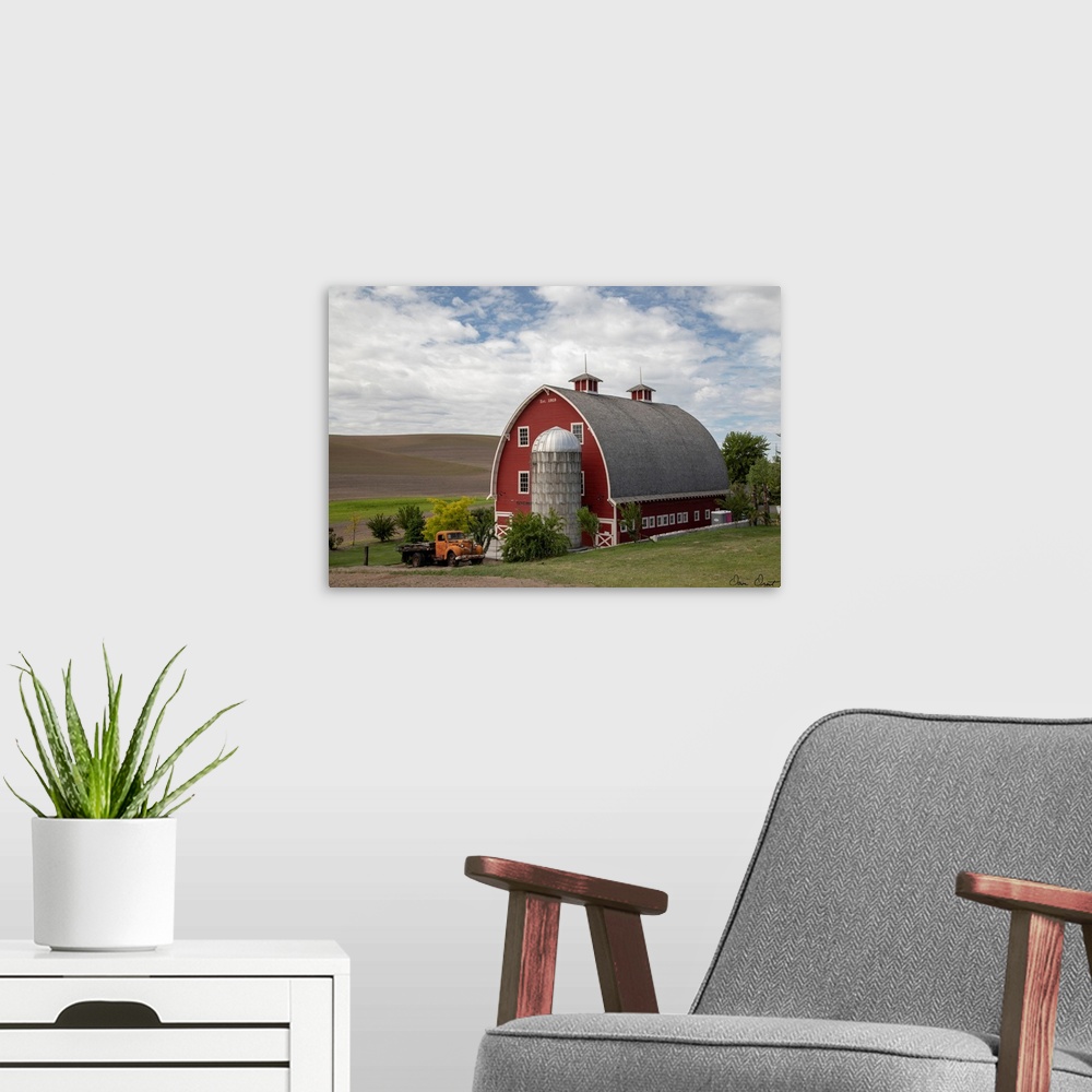 A modern room featuring A photograph of a large red barn and grain silo with a vintage orange truck parked out front