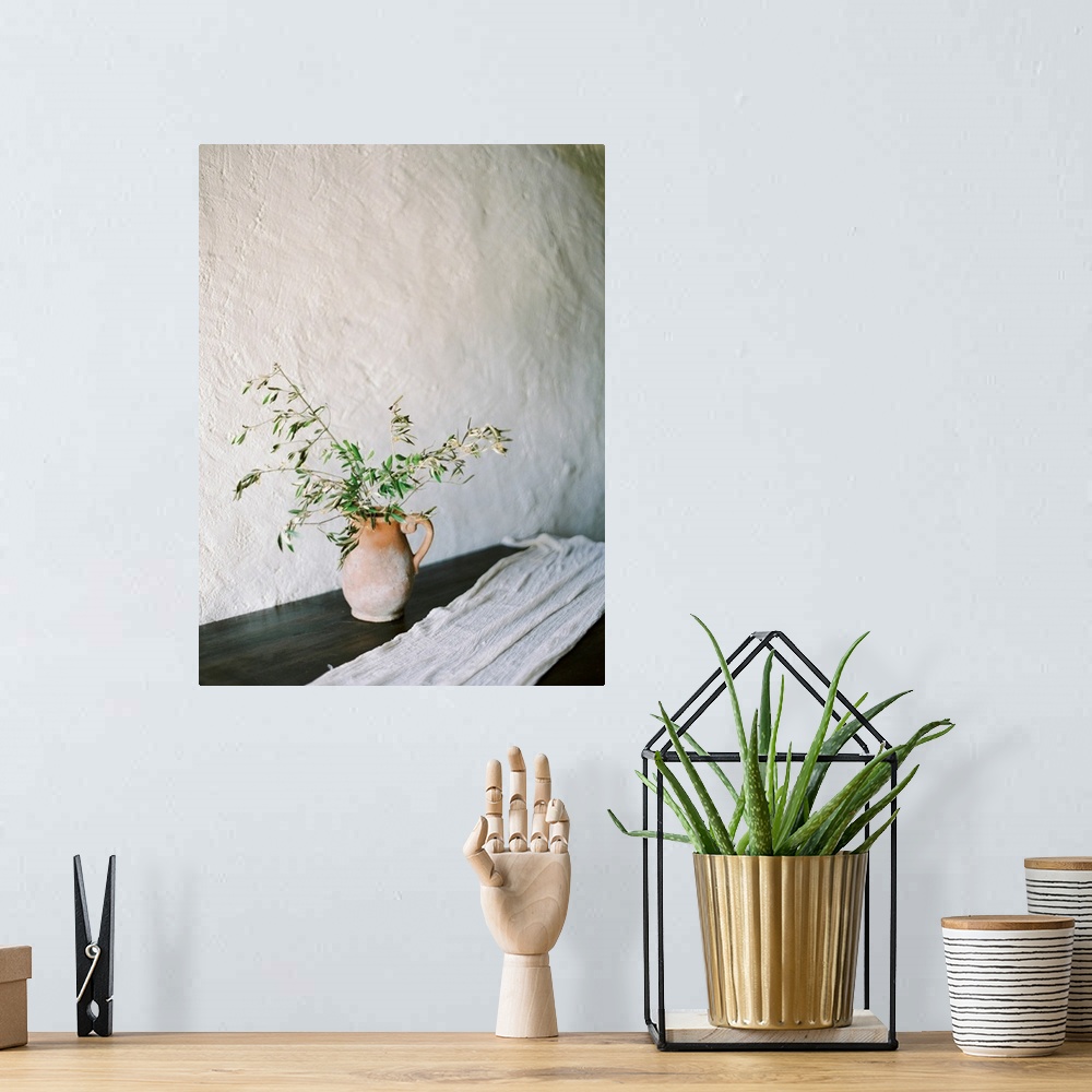 A bohemian room featuring A photograph of olive branches in a clay jug in a simple indoor mediterranean setting.