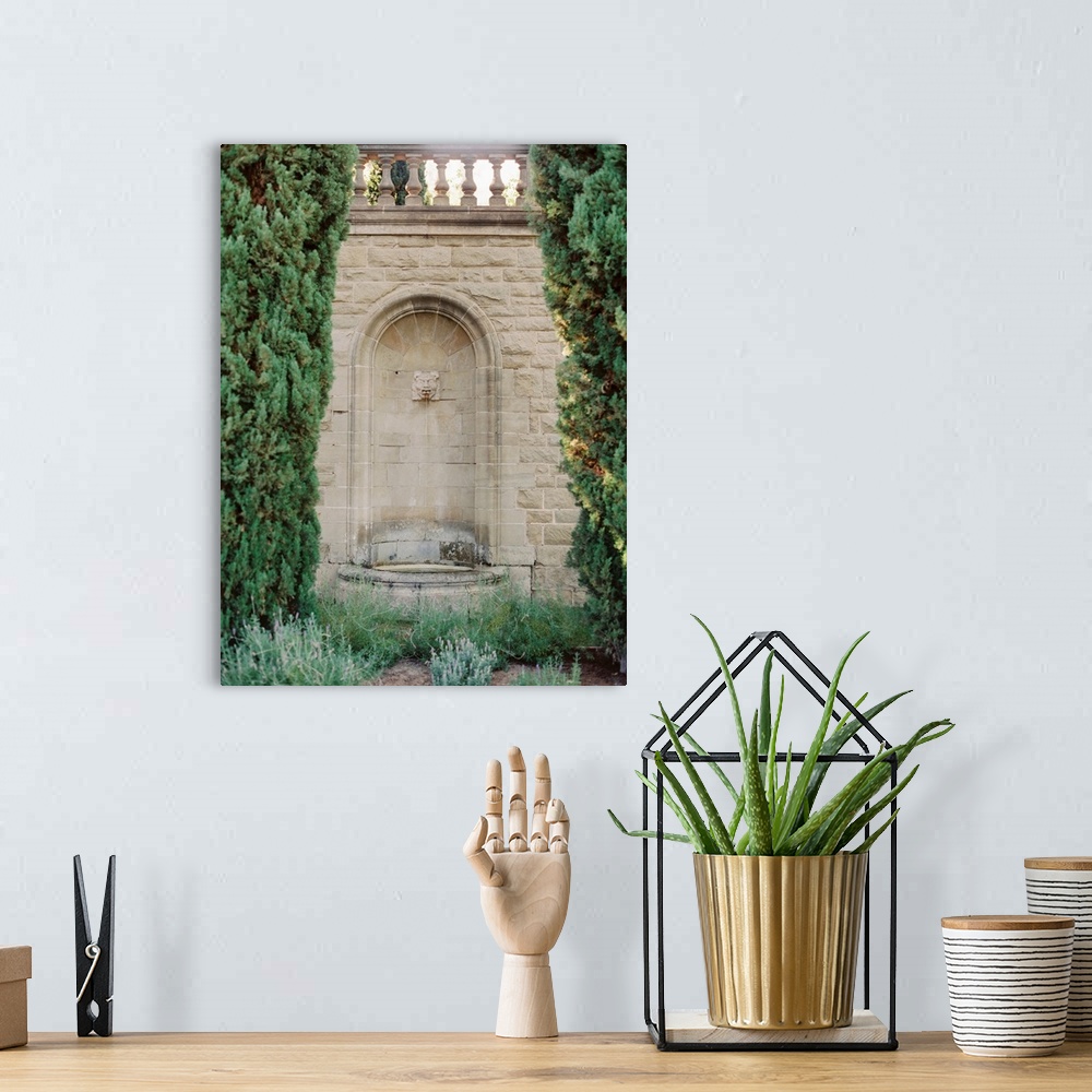 A bohemian room featuring A photograph of an ornate fountain set into the wall amidst elegant gardens of a Mediterranean vi...