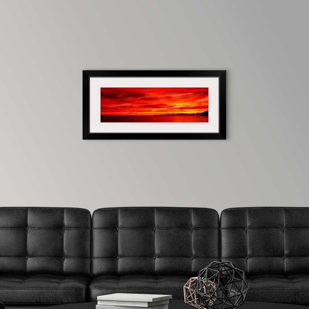 A modern room featuring Large wall image of a deep warm sunset over the ocean with a little strip of land on the right si...