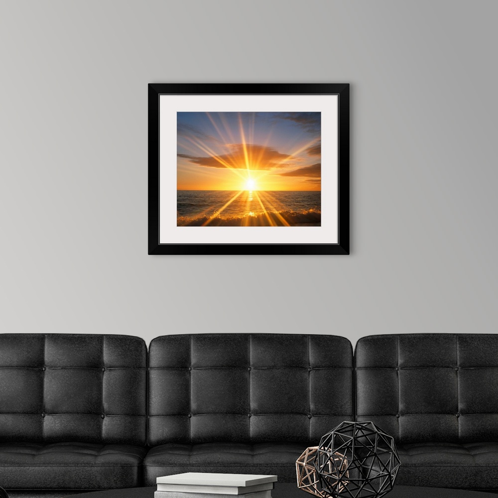 A modern room featuring Giant photograph of a bright sunset reflecting onto an ocean as the waves crash against a sandy b...