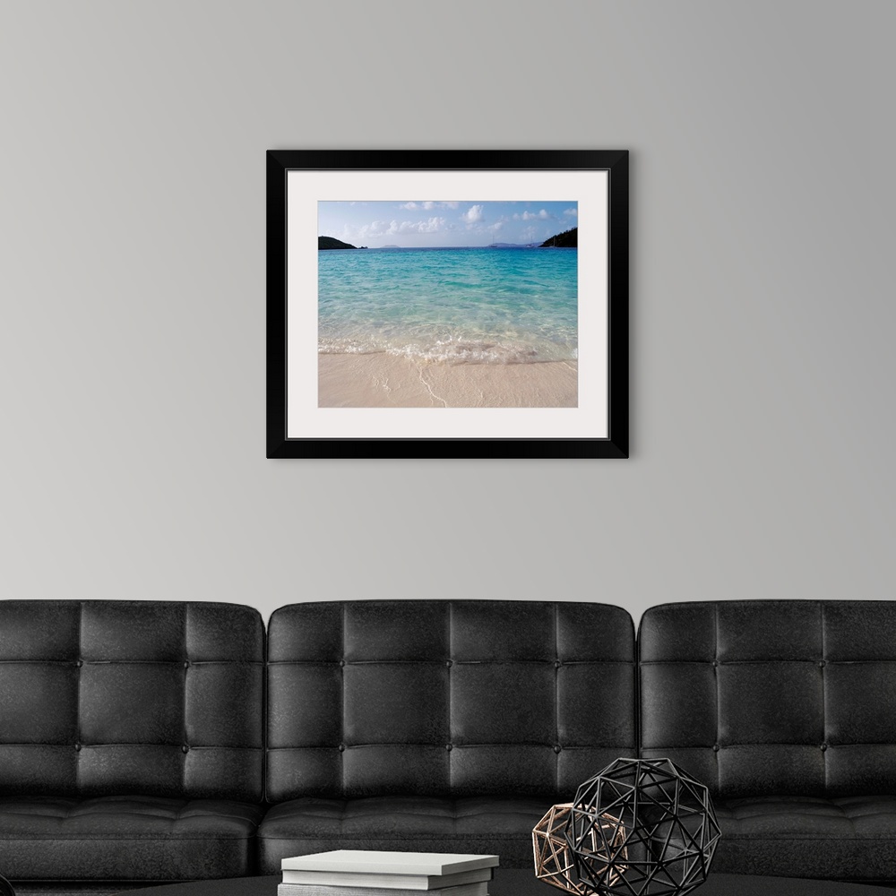 A modern room featuring Big photograph focuses on the waves of a cove gently rolling back into sea as a few boats and lan...