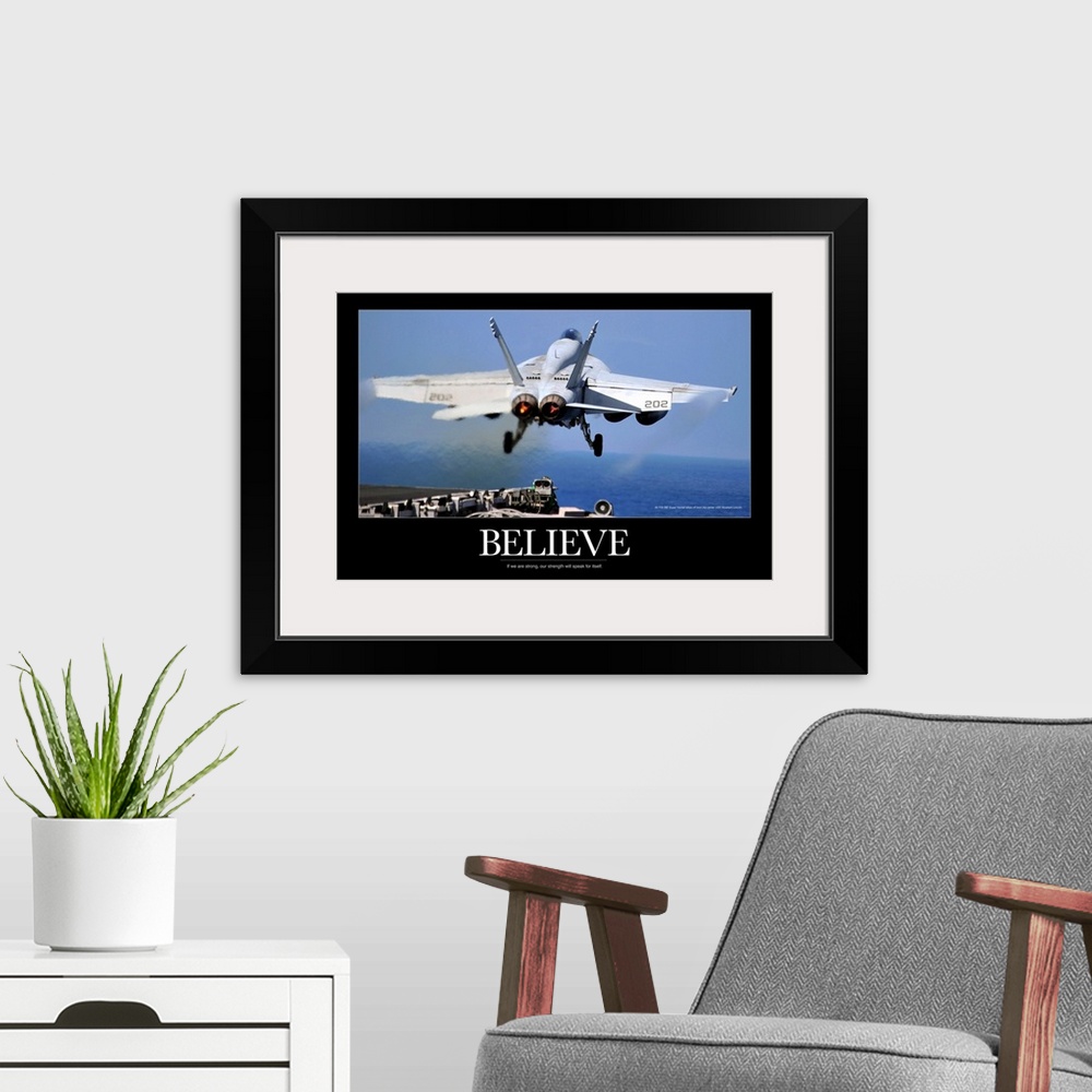 A modern room featuring Large poster of a jet taking off from a ship with a black border around the picture and the word ...