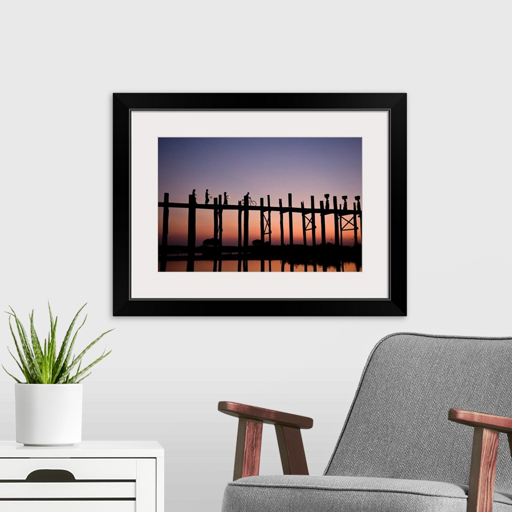 A modern room featuring Photograph of people walking and biking across a bridge made of tall wooden beams over the ocean ...