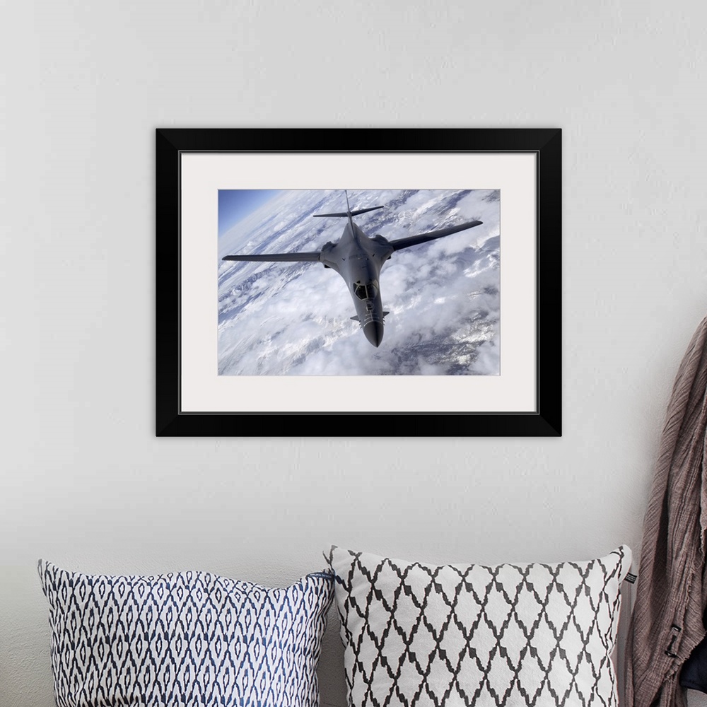 A bohemian room featuring A military aircraft is photographed flying above the clouds and over snowy mountainous terrain.