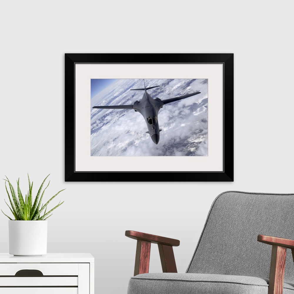 A modern room featuring A military aircraft is photographed flying above the clouds and over snowy mountainous terrain.