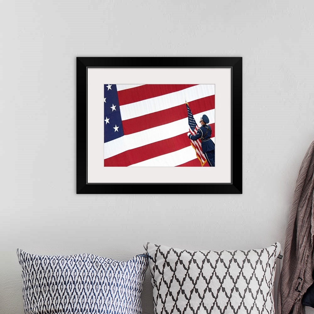 A bohemian room featuring A soldier stands in front of a massive American flag while holding a smaller flag during the chan...