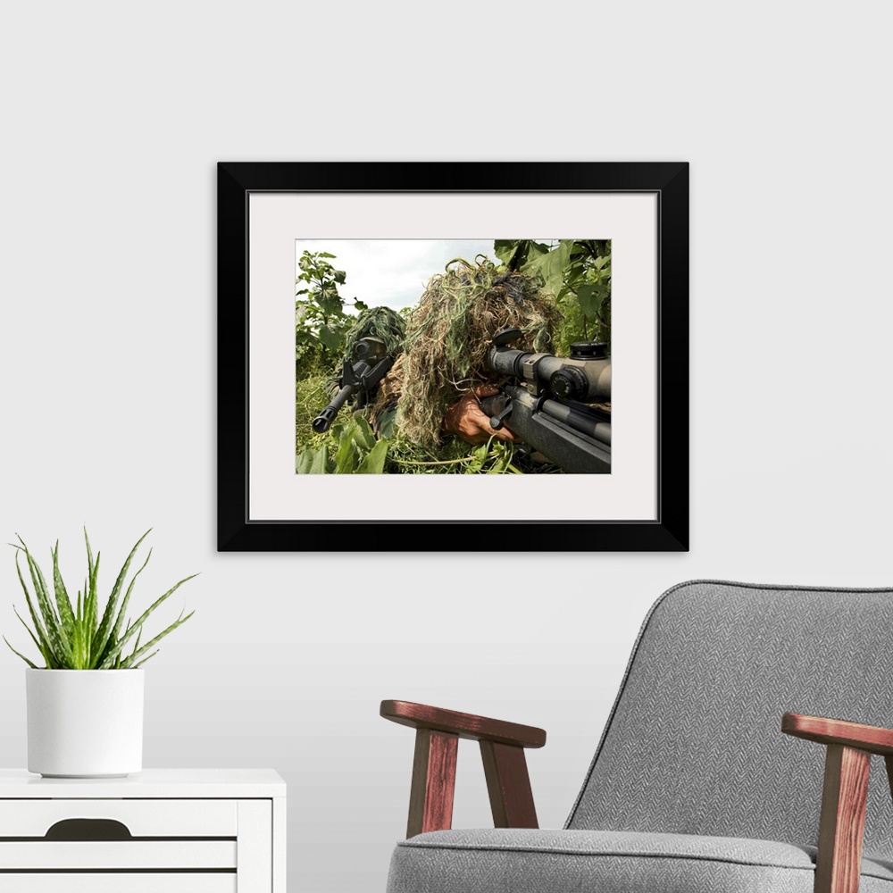 A modern room featuring Military photo of two men lying on their stomachs in the grass, covered in ghilie suits to comofl...