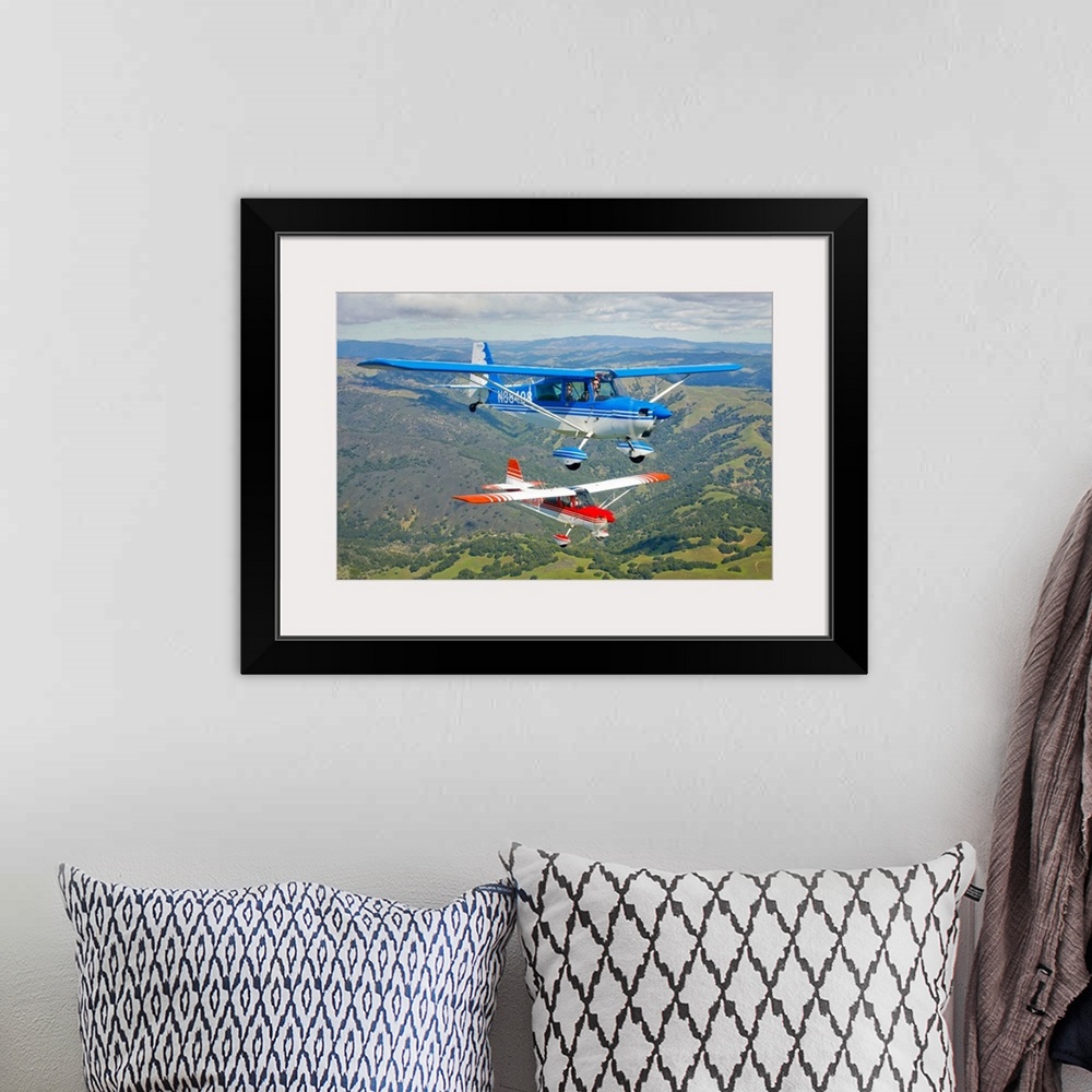 A bohemian room featuring Two small airplanes are photographed while in flight over vast open land.