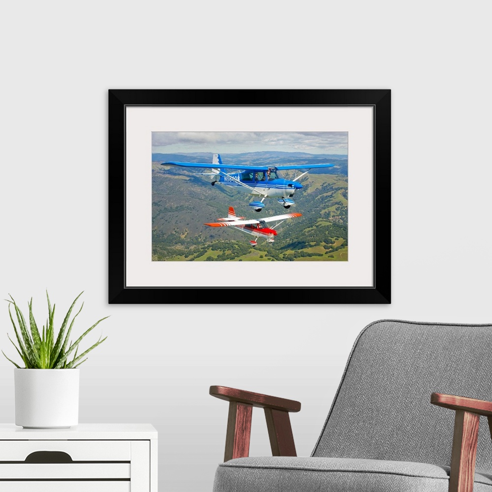 A modern room featuring Two small airplanes are photographed while in flight over vast open land.