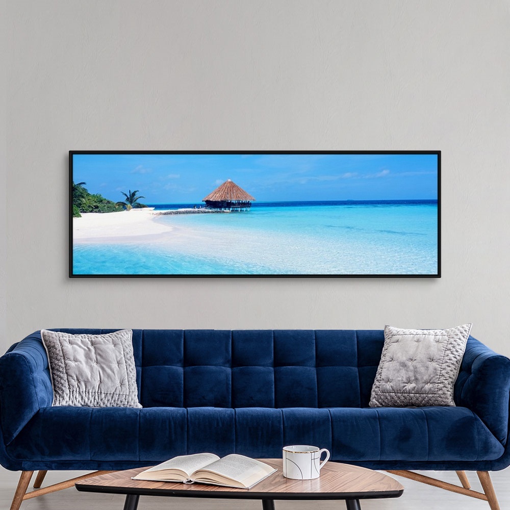 A modern room featuring Panoramic photograph displays a small hut sitting on a sandy piece of coastline within the crysta...
