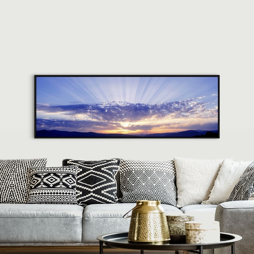 A bohemian room featuring This panoramic wall art captures as a photograph radiant sun beams radiate from behind clouds ove...