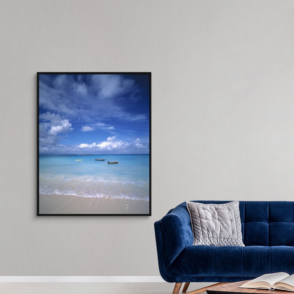 A modern room featuring Huge photograph showcases a group of three small water vessels anchored near the shore of a sandy...