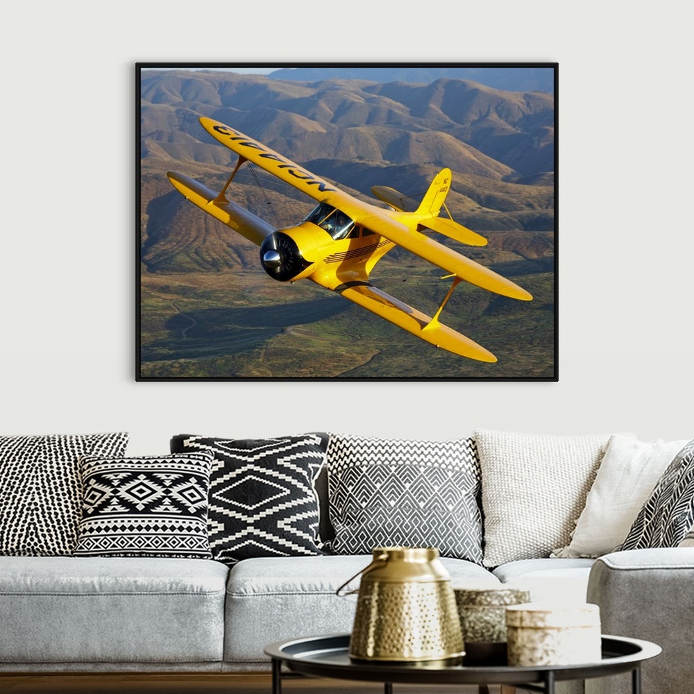 A bohemian room featuring Photograph of a Beechcraft D-17 Staggerwing single propeller biplane flying over rolling hills.
